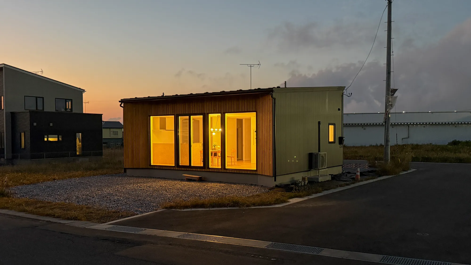 夕焼けの空の下で窓の明かりが灯る木の外壁の平屋(階上)|HOUSE EN のデザイン